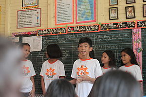 Sechs Kinder stehen vor einer Tafel und sprechen zur Klasse.