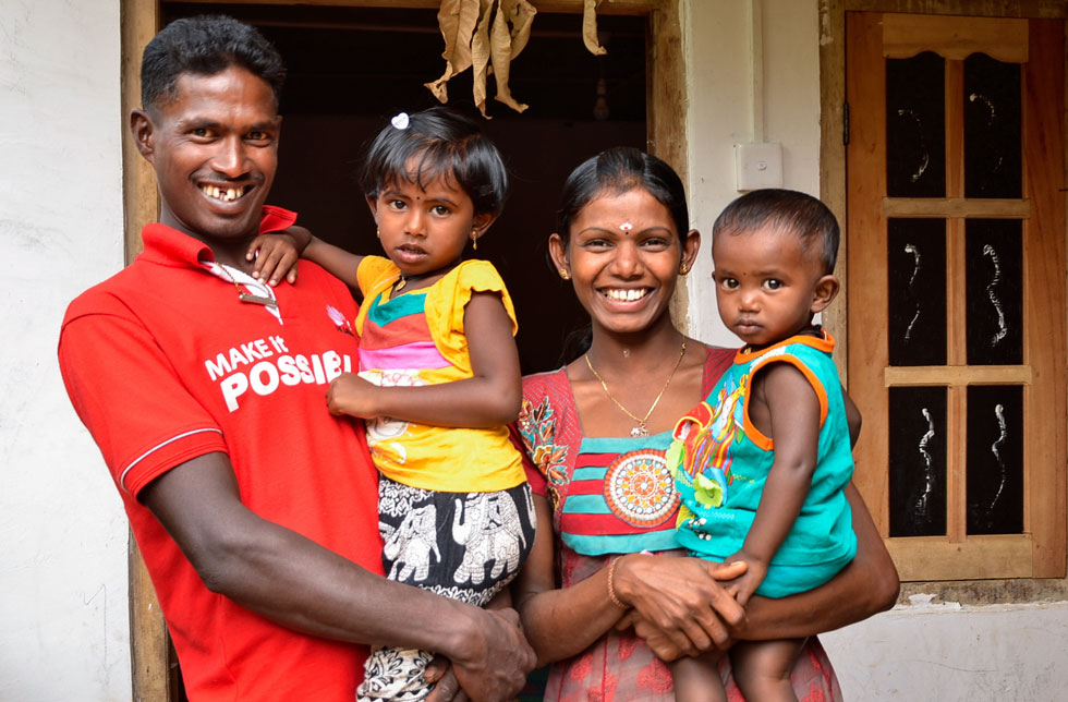 Ein Vater und eine Mutter in Sri Lanka umarmen lächelnd ihre Kinder.