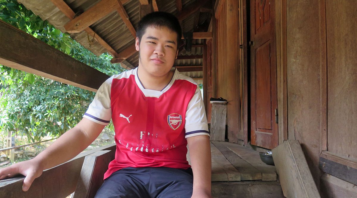 Vietnam: Ein Junge in einem Fussballshirt sitzt auf der Holztreppe vor seinem Haus.