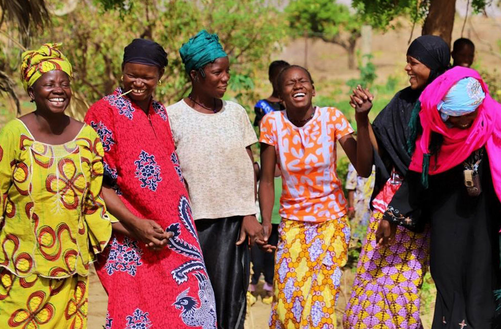 Afrika, Mali: Ein Gruppe Frauen tanzen Hand in Hand. Sie tragen bunte, traditionelle Kleidung und lachen.