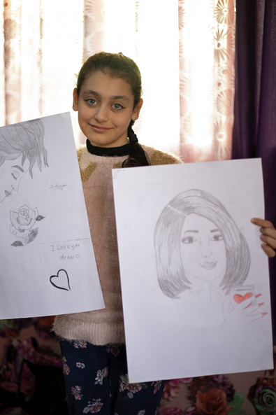 Syrien: Ein Mädchen hält selbstgezeichnete Bilder von Frauen in die Kamera.