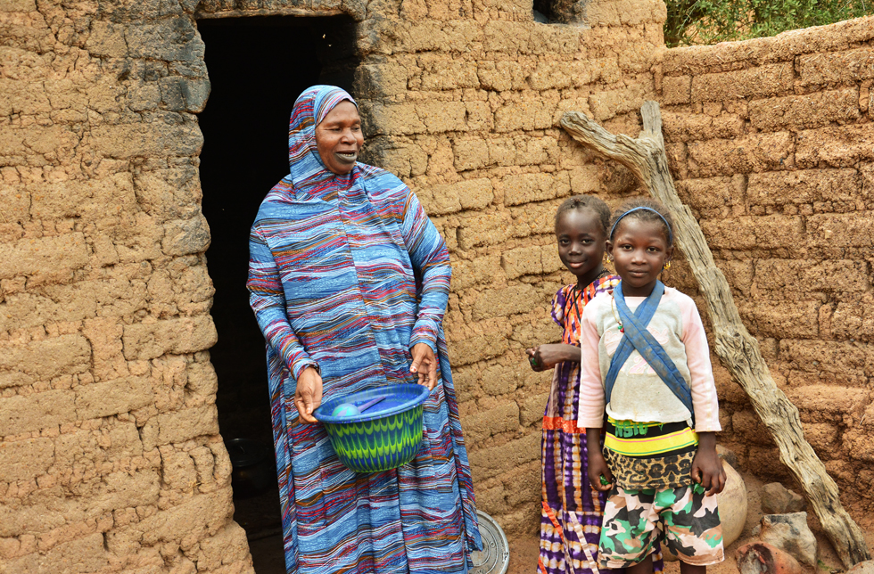 Die Grossmutter und die beiden kleinen Mädchen stehen vor ihrem Haus in Mali.