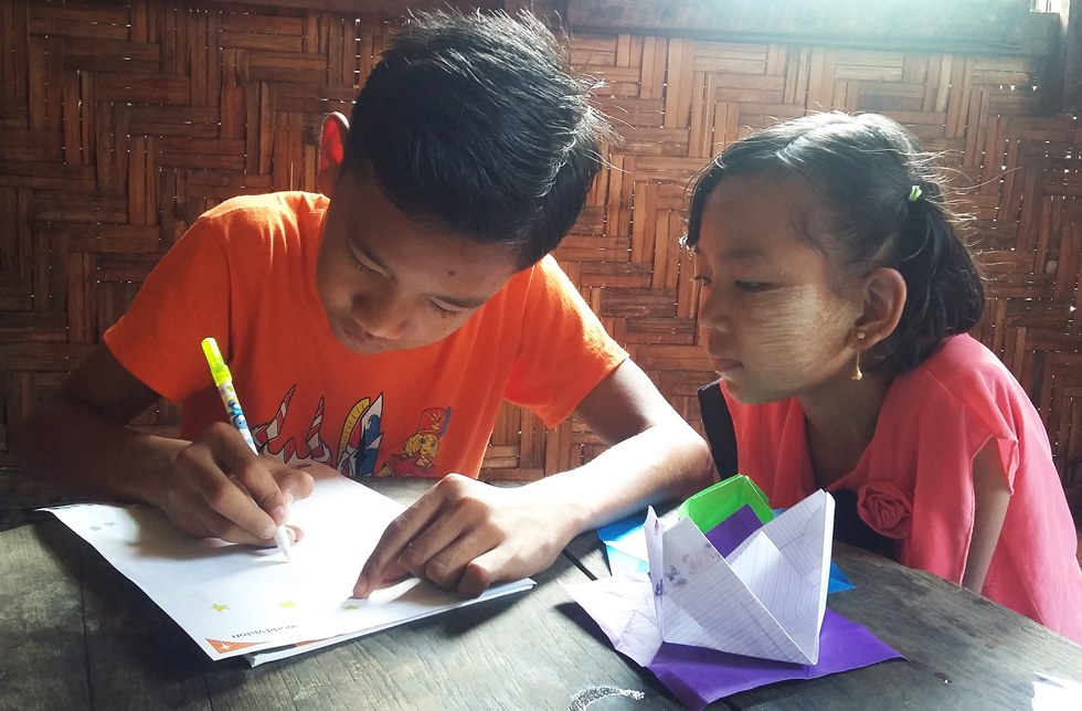 Ein Junge in Myanmar schreibt seinem World Vision-Paten einen Brief. Seine Schwester schaut zu.
