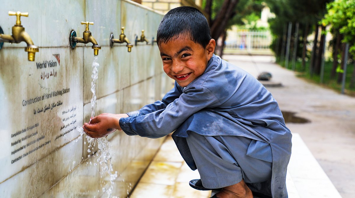 Afghanistan: Ein Junge wäscht sich die Hände an einer von World Vision eingerichteten Wand mit vielen Wasserhähnen.