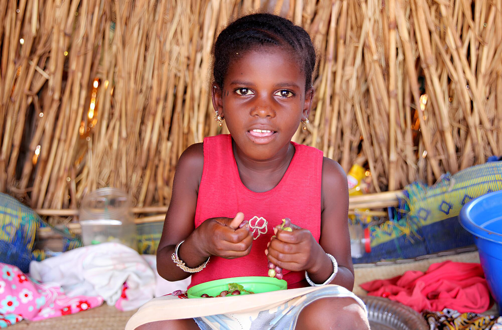 Mali: Ein Mädchen sitzt auf dem Boden und isst Trauben.