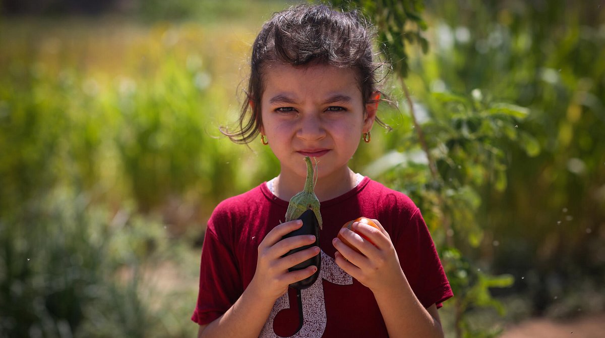 Irak: Ein Mädchen hält eine Aubergine und eine Tomate in den Händen.