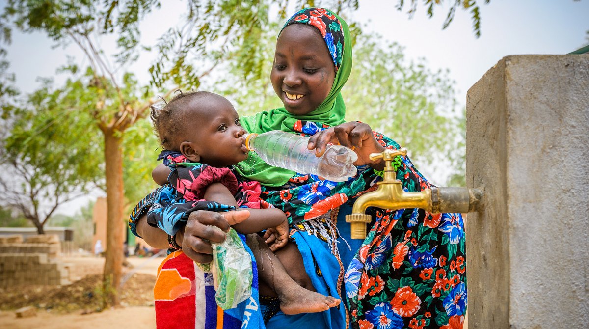 Niger: Eine junge Frau gibt einem Kleinkind aus einer Flasche Wasser aus dem Brunnen zu trinken.