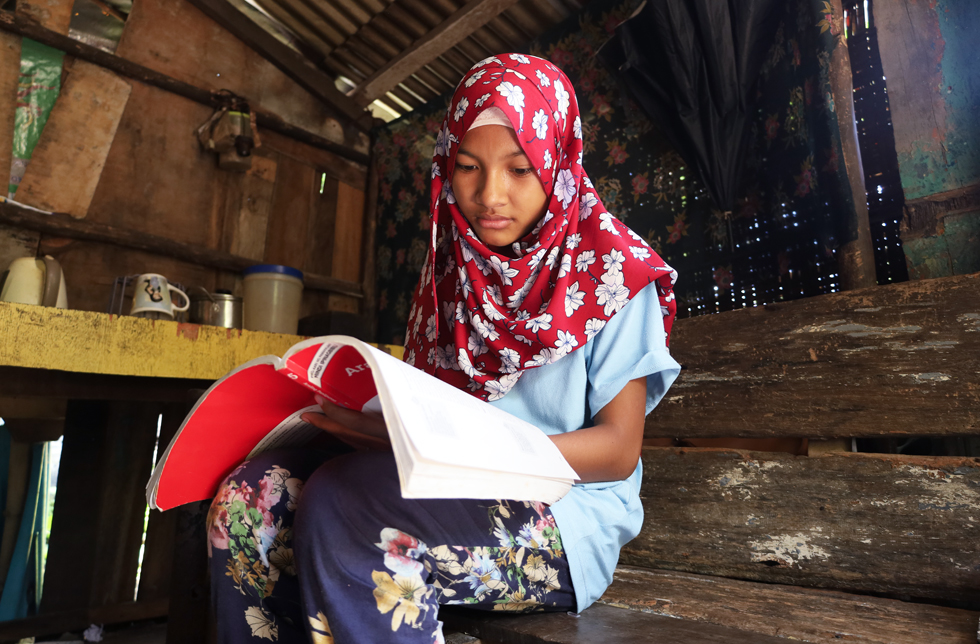Philippinen: Ein Mädchen sitzt in einer einfachen Hütte mit ihrem Schulbuch auf einer Bank.
