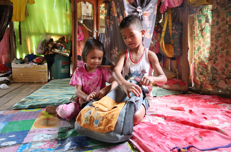 Philippinen: Zwei Kinder sitzen im Haus und bestaunen einen Schulrucksack.