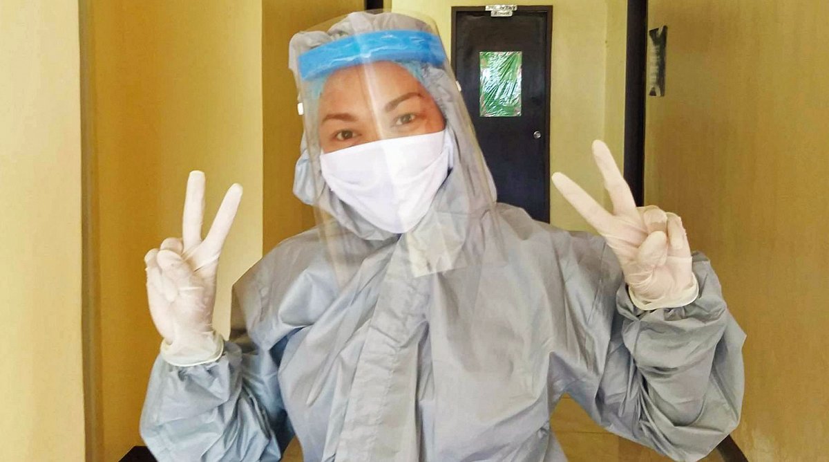 Eine Hebamme in Schutzanzug und Maske steht in einem Krankenhausflur in den Philippinen und gibt das “Victory”-Zeichen.