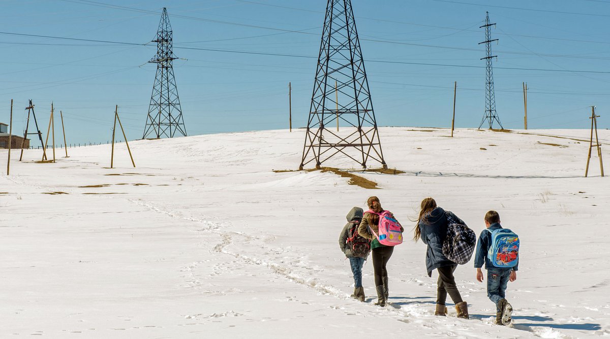 Armenien: Verschneite Landschaft mit Strommasten auf dem Feld. Blauer Himmel. Zwei Jungen und zwei Mädchen stapfen durch den Schnee.