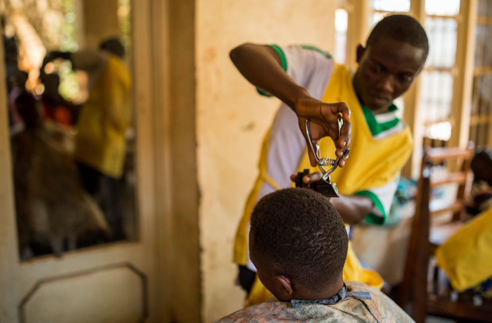 Demokratische Republik Kongo/DRK/DRC: Ein Mann in einem gelben T-Shirt schneidet die Haare eines anderen Mannes.