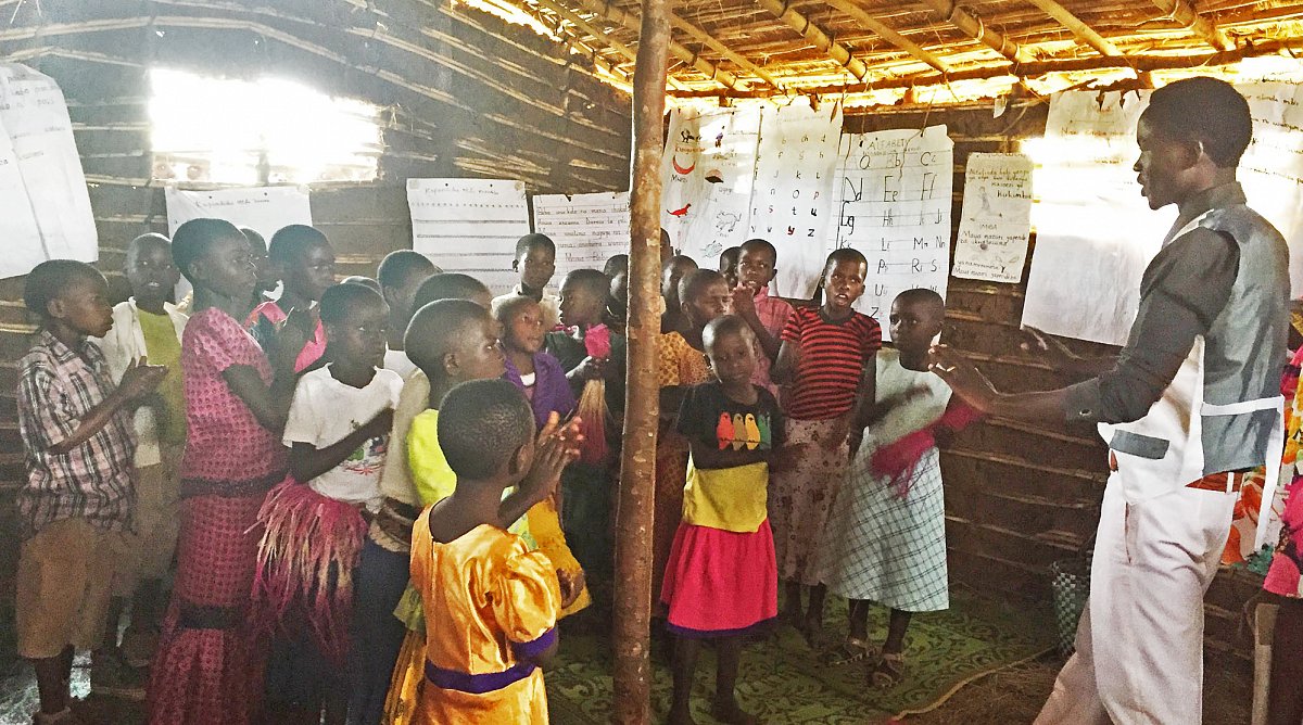 Gruppe Kinder mit Lehrer in einer Strohhütte am Singen.