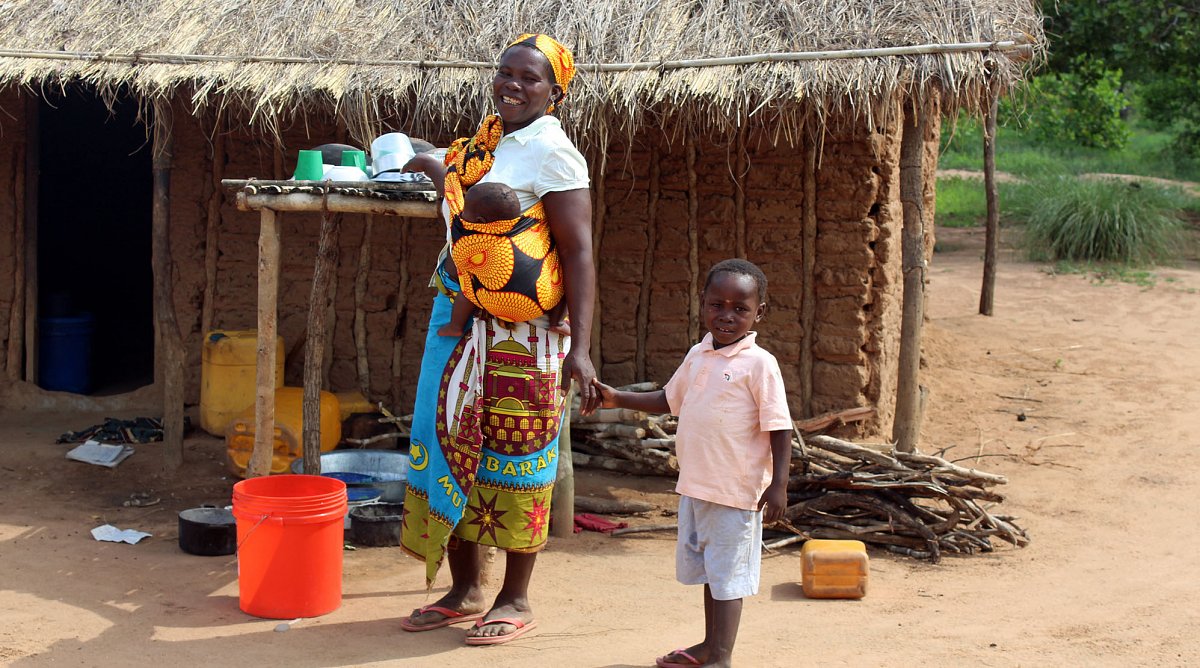 Mutter und zwei Kinder in Mosambik vor einer Hütte