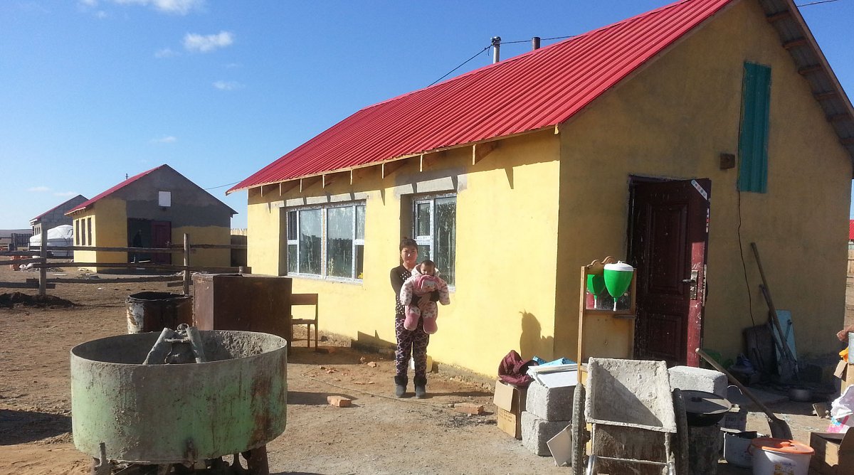 Frau und Kleinkind in der Mongolei stehen vor einer Baustelle eines Hauses.