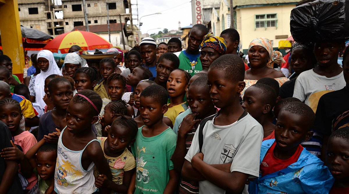 Auf der Strasse lauschen Kinder und Erwachsene den Erklärungen von World Vision-Mitarbeitenden über Ebola