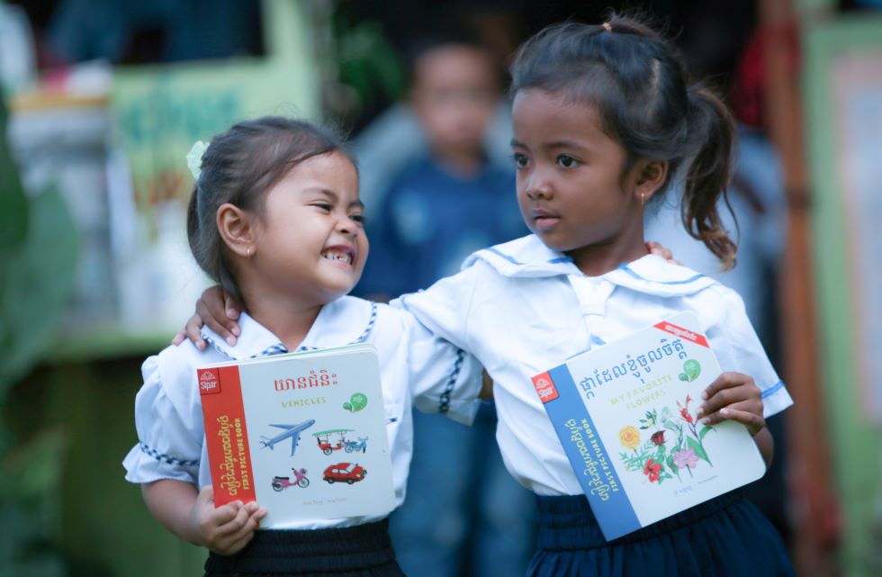 Zwei Mädchen in Kambodscha freuen sich über neue Lehrbücher für die Vorschule.