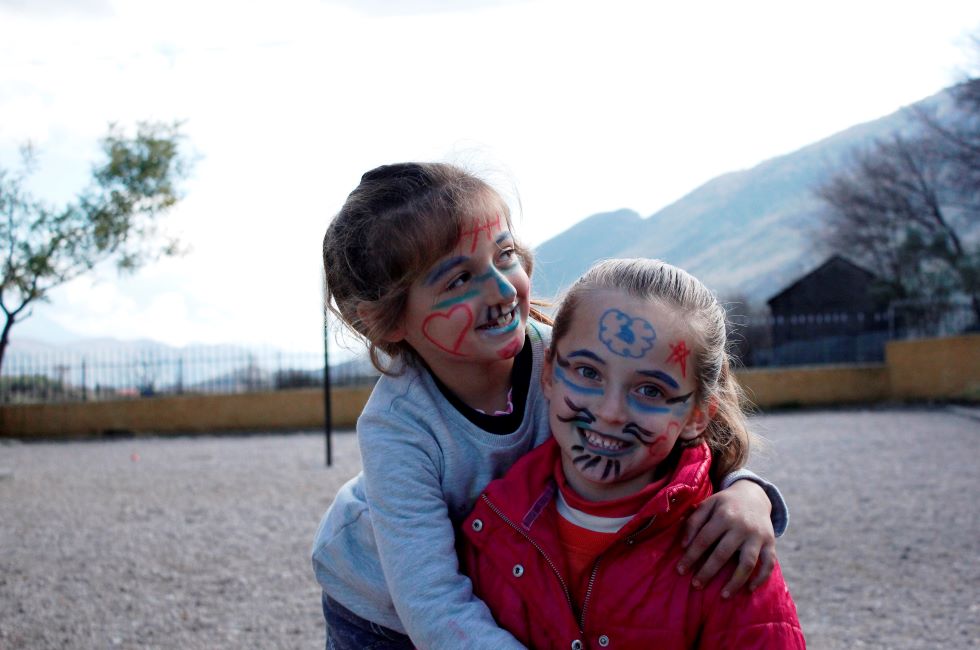 Albanien: Zwei junge Mädchen mit bemalten Gesichtern umarmen sich und lachen