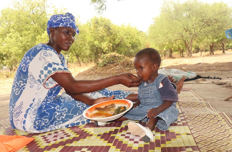 Südsudan: Eine Mutter und ihr Sohn sitzen auf einer Decke, sie füttern ihn mit der Hand von einem Teller. 