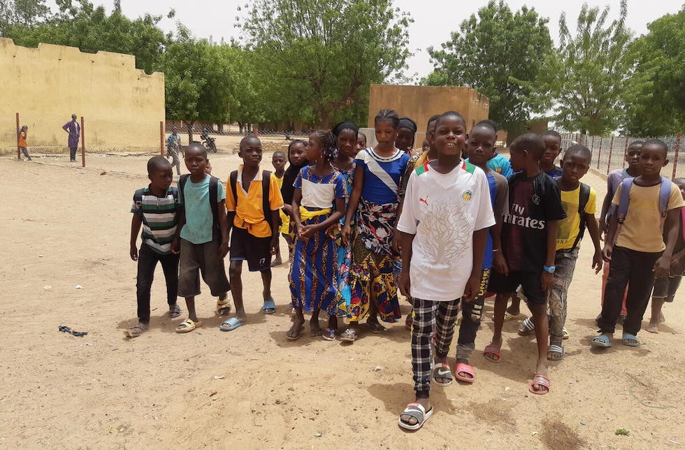Mali: Eine Gruppe Schulkinder steht auf einem Schulhof und bewegt sich auf die Kamera zu. Hinter ihnen ist ein Zaun zu erkennen.