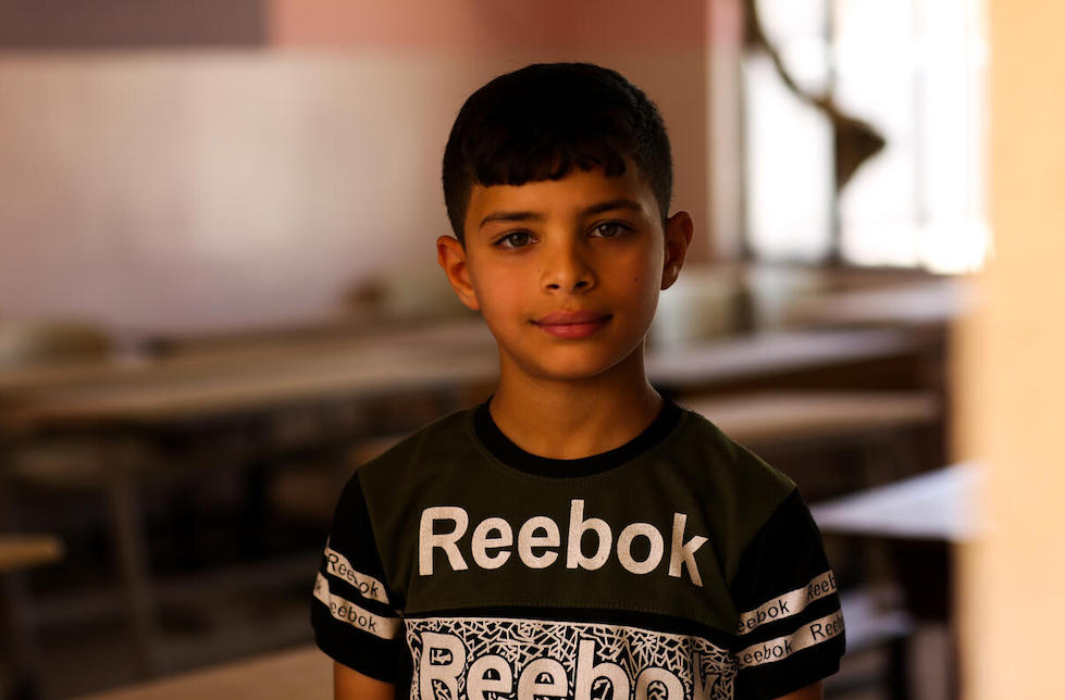 Irak: Porträt eines Jungen. Er trägt ein Reebok-Shirt, hinter ihm ist unscharf ein Klassenzimmer zu erkennen.