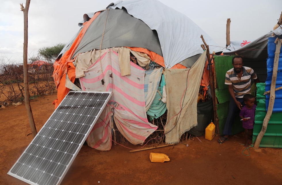 Somalia: Ein Mann und ein Kind kommen aus einem behelfsmässigen Haus, vor  dem ein Solarmodul steht.