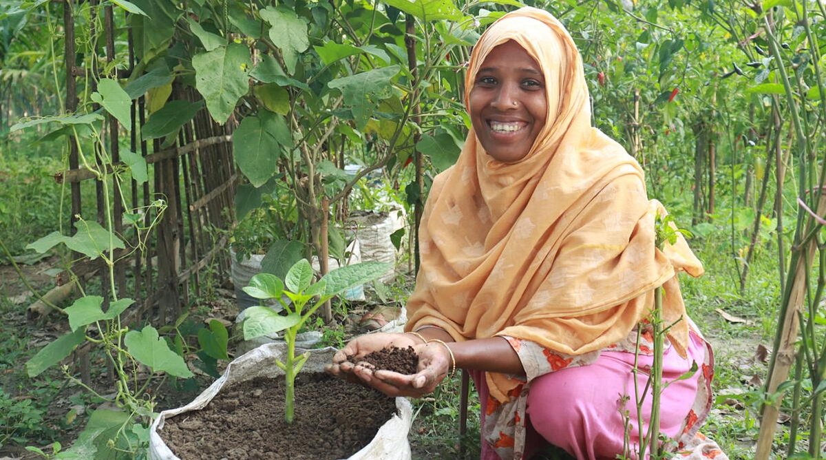 Bangladesch: Wurmkompost-Produzentin Monowara Begum sitzt in einem Gemüsefeld vor einem Sack voller Erde. Sie hält die Erde in der Hand.