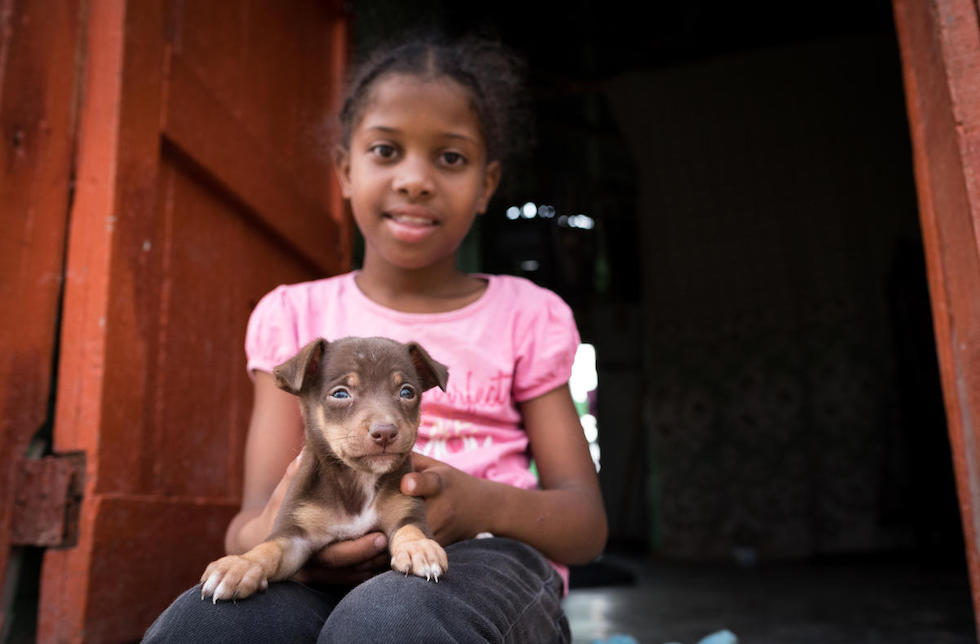 Dominikanischen Republik: Ein junges Mädchen sitzt in der Tür und hat einen kleinen Welpen auf dem Schoss.