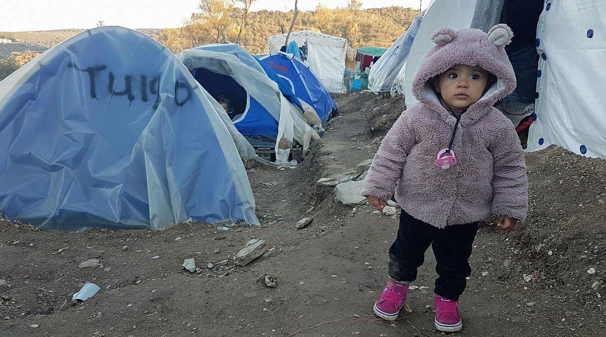 Moria auf Lesbos, Griechenland: Ein Mädchen steht, eingepackt in einer warmen Jacke, vor einem Zelt in einem Flüchtlingslager.