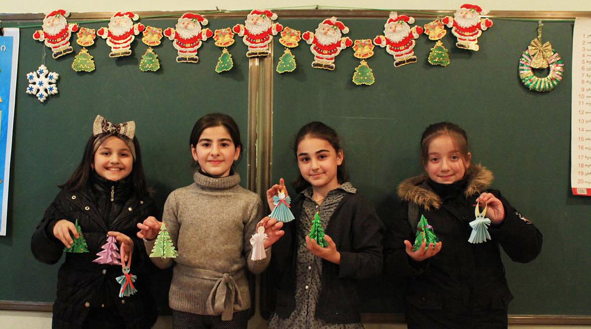 Vier Mädchen stehen vor einer Schultafel und halten gebastelten Weihnachtsschmuck in die Kamera.