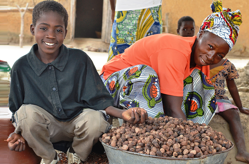 Eine Junge hilft seiner Mutter beim Auslesen von Nüssen in Neguela, Mali