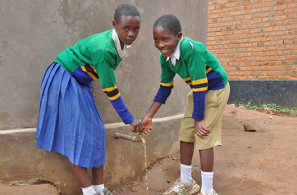Zwei Kinder stehen vor einem Wassertank, der das Dorf mit sauberem Wasser versorgt. In Mbuka, Tansania 