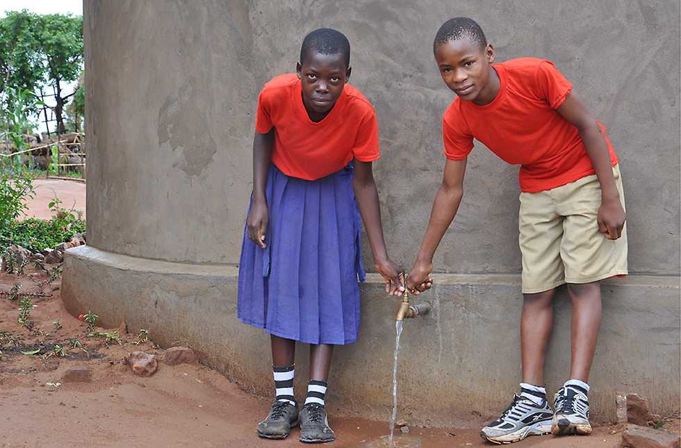 Zwei Kinder zeigen den Zugang zu sauberem Trinkwasser in ihrem Dorf in Mbuka, Tansania