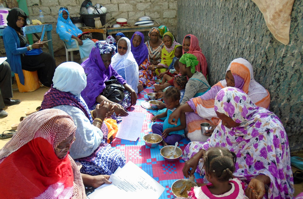Mauretanische Mütter sitzen in einem Hof und füttern ihre Kleinkinder mit einem Gemüsebrei.