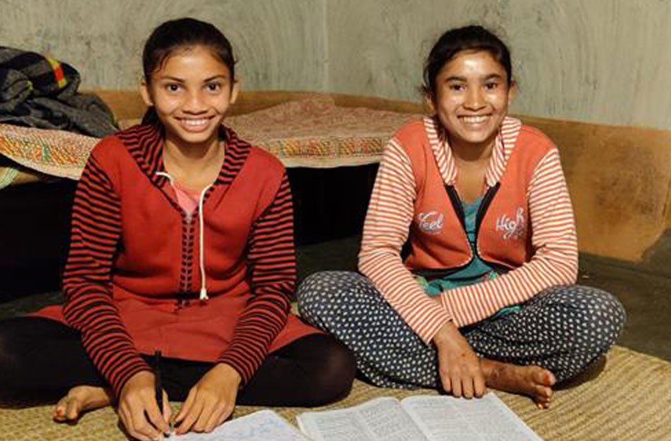 Indien: Zwei Mädchen sitzen auf dem Boden und lösen Hausaufgaben.