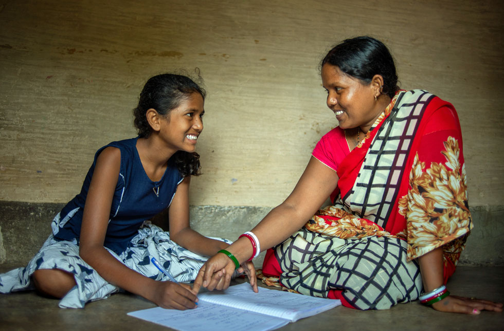 Indien: Eine indische Schülerin zeigt ihrer Mutter ihre Hausaufgaben.
