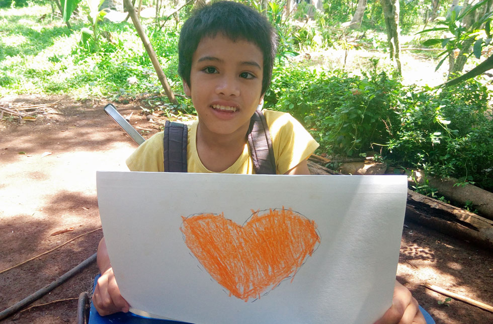 Ein Junge hält ein gemaltes Herz in leuchtendem Orange hoch.