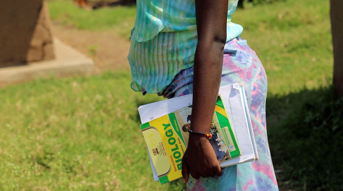 Afrika: Eine schwangere Frau hält Schulbücher in den Händen.
