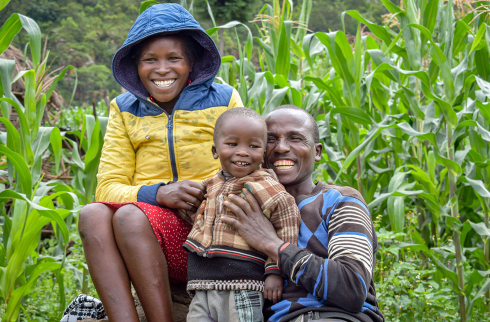 Ein Vater und eine Mutter in Kenia umarmen lachend ihr Kind.