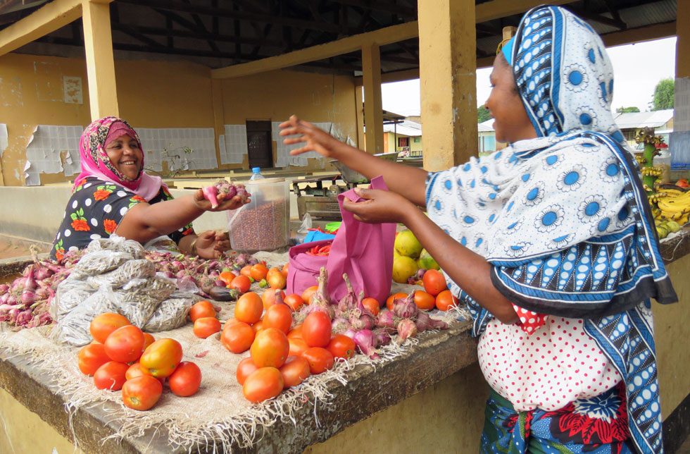 Eine afrikanische Frau verkauft einer anderen Frau Gemüse an einem Marktstand.