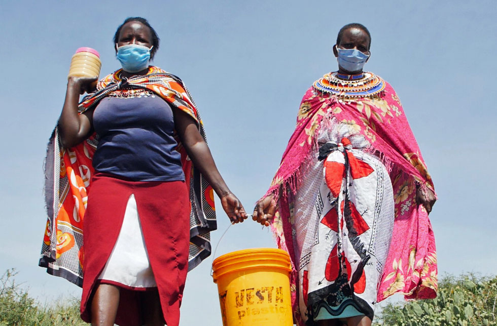 Zwei Frauen in Kenia tragen zusammen einen Honigeimer.