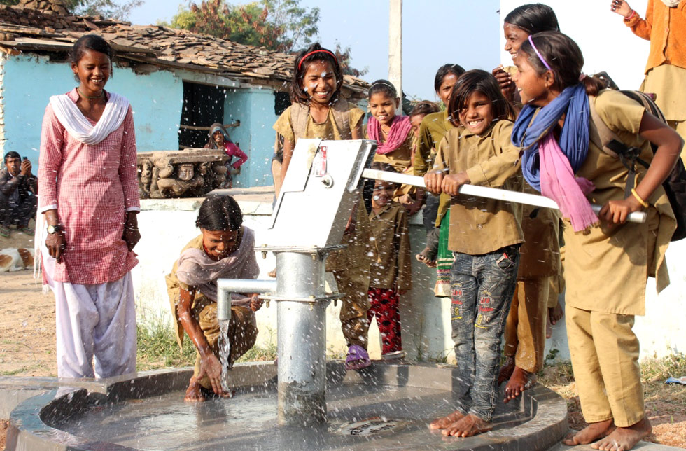 Einige Kinder in einem indischen Dorf spielen fröhlich mit dem neuen Trinkwasserbrunnen.