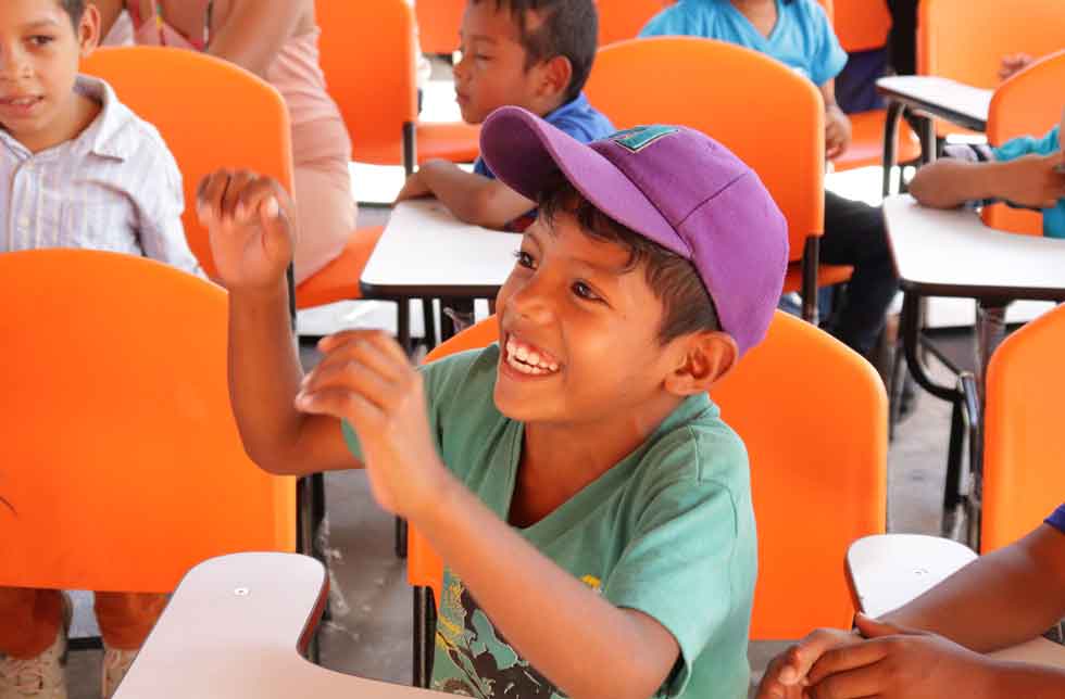 Eine Schuljunge in La Guajira, Kolumbien, sitzt lachend im Klassenzimmer.