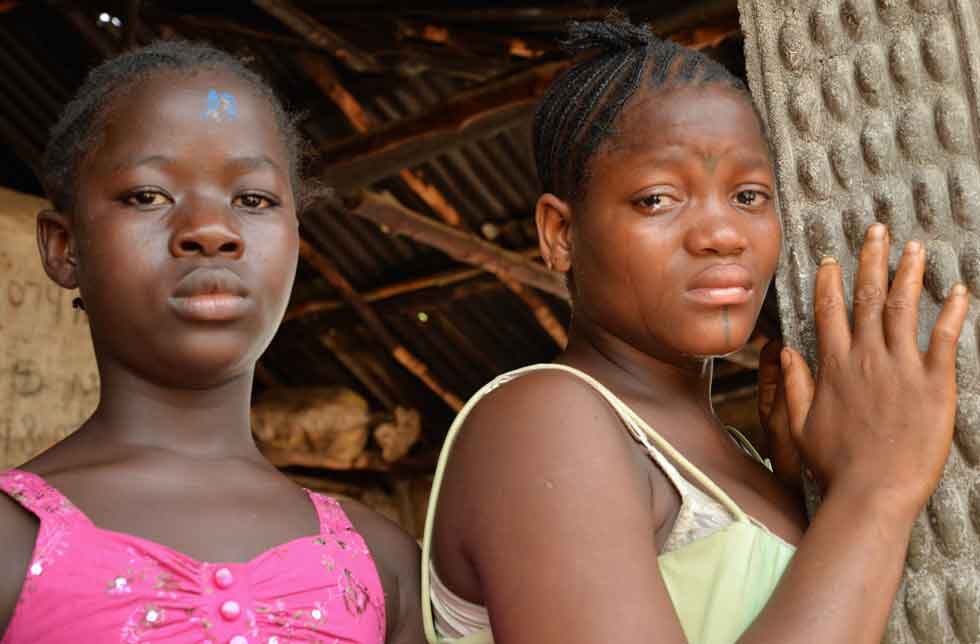 Sierra Leone: Zwei junge Mädchen schauen traurig direkt in die Kamera, eines weint. Sie stehen im Eingang einer Hütte.