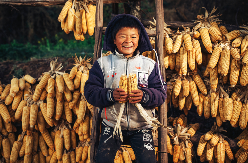 Ein chinesischer Junge steht vor einem Gestell mit trocknenden Maiskolben.