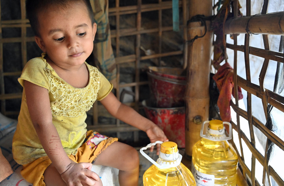 Bangladesch: Ein Mädchen sitzt in einer einfachen Hütte und spielt mit Speiseölflaschen.