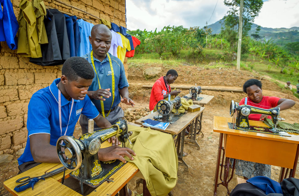 Ruanda: Eine Mann erklärt seinen Mitarbeitenden an den Nähmaschinen wie man Uniformen näht.