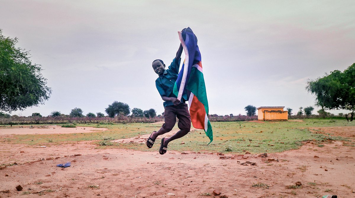 Südsudan: Ein Junge mit der Landesflagge in der Hand springt in die Höhe.