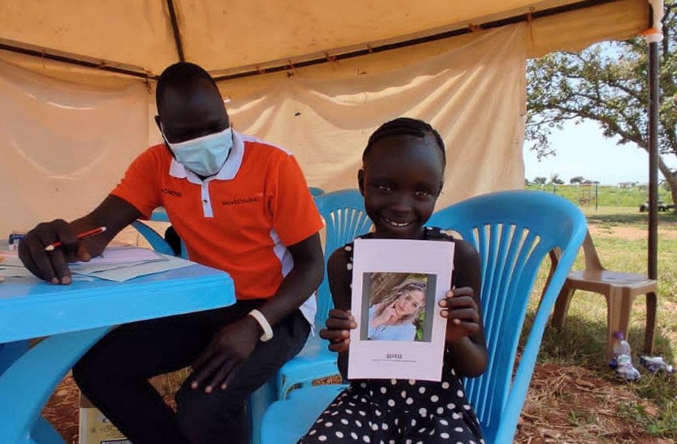 Uganda: Ein Kind hält das Foto seiner Patin in den Händen und lächelt.
