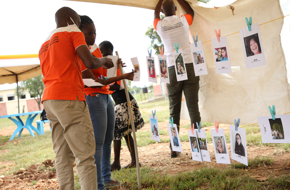 Uganda: Mitarbeitende von World Vision hängen Fotos von Patinnen und Paten auf.